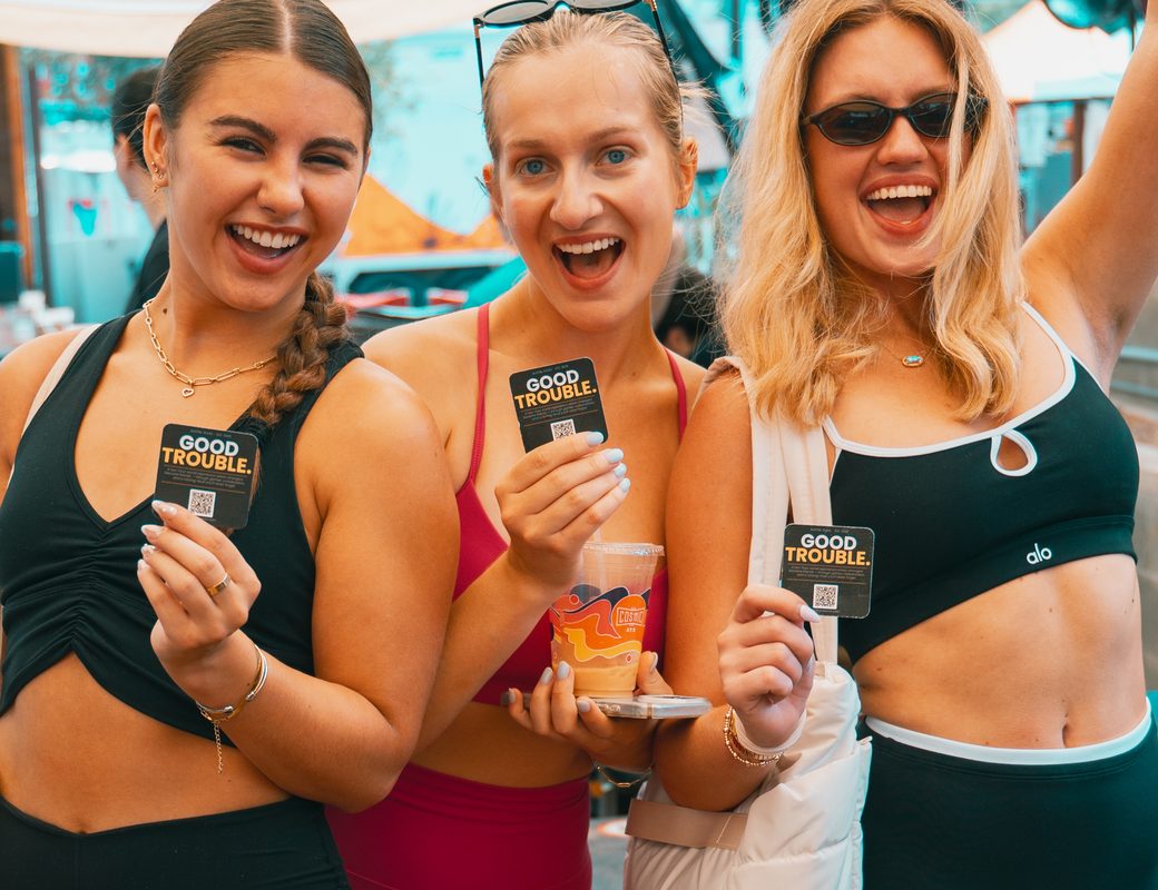 Three friends holding Sweaty Friends cards at an event